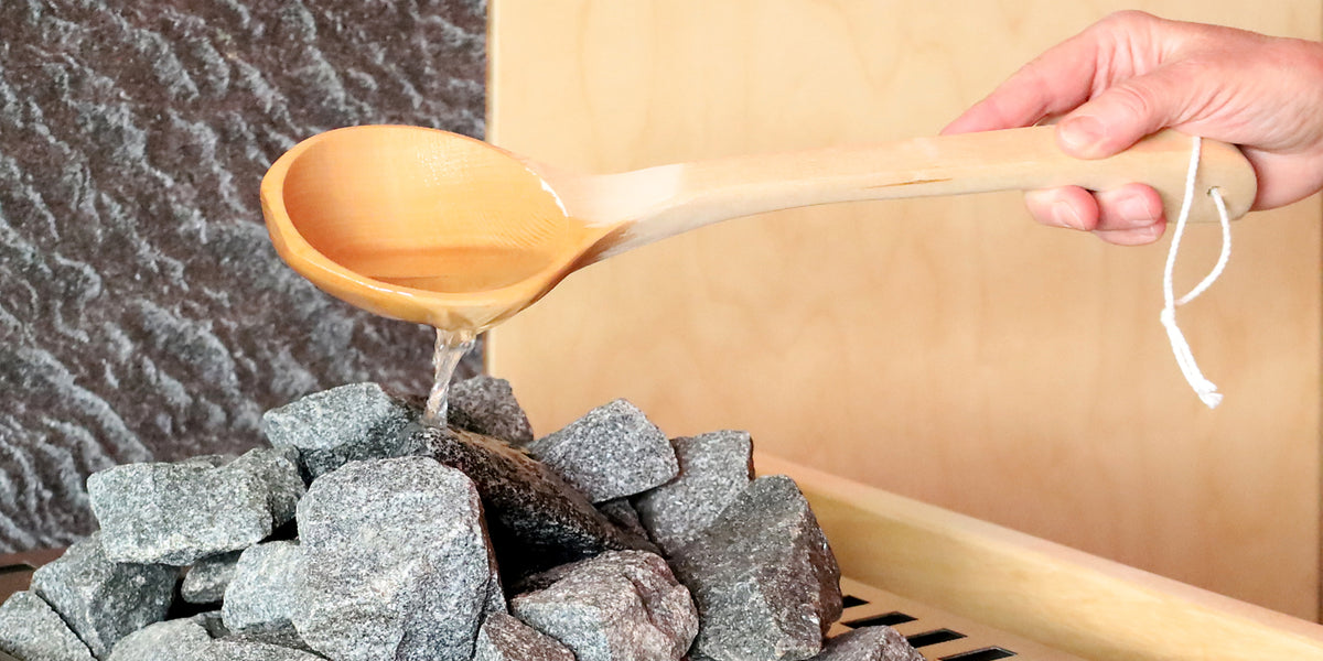 Saunaaufguss mit Holzkelle über Saunasteine
